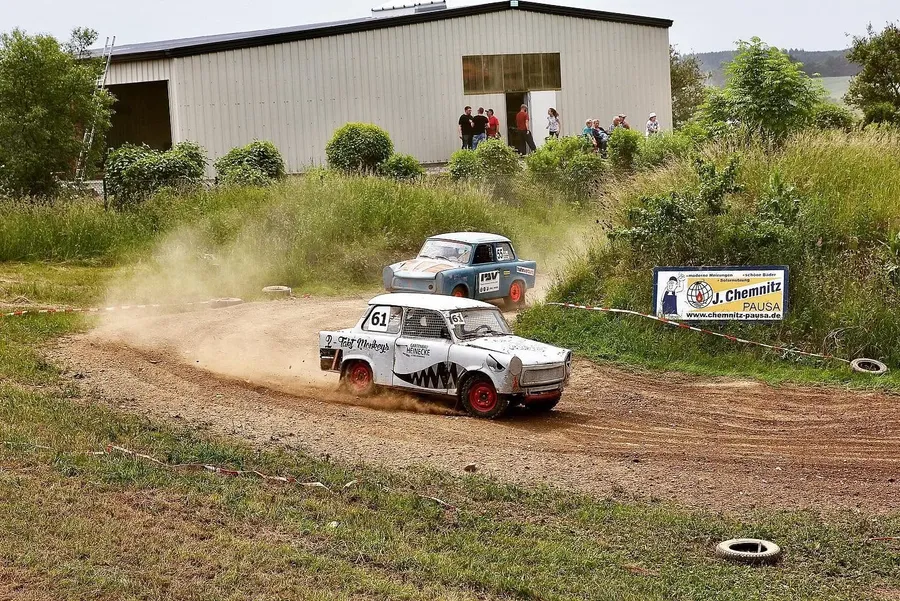 Trabant mit der Startnummer 61 driftet in einer Staubwolke durch eine Kurve, dahinter ein hellblauer Trabant mit der Startnummer 55