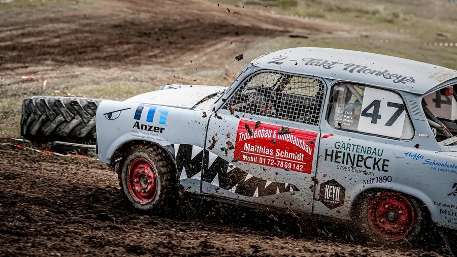 Grauer Trabant mit der Startnummer 47 und aufgemaltem Haifischgebiss wirft auf schlammiger Strecke Erde auf