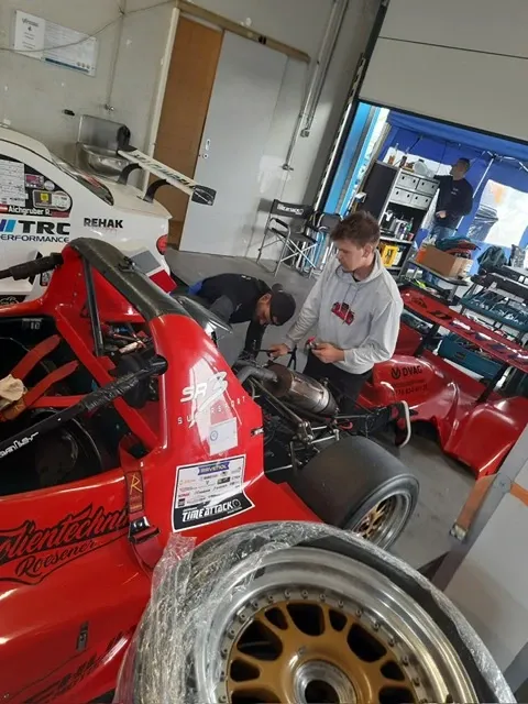 Zwei Personen arbeiten in der Werkstatt am roten Radical SR3, im Hintergrund ein zweites Fahrzeug und Werkzeug