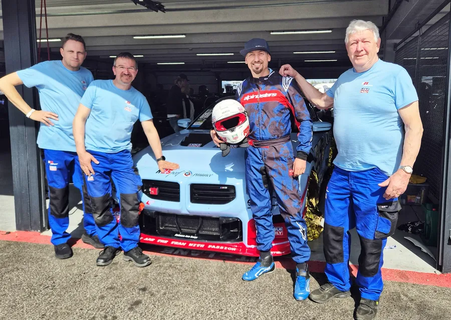 Vier Mitglieder des Teams R25Performance vor dem BMW M2 in der Box, einer davon im Rennanzug mit Helm