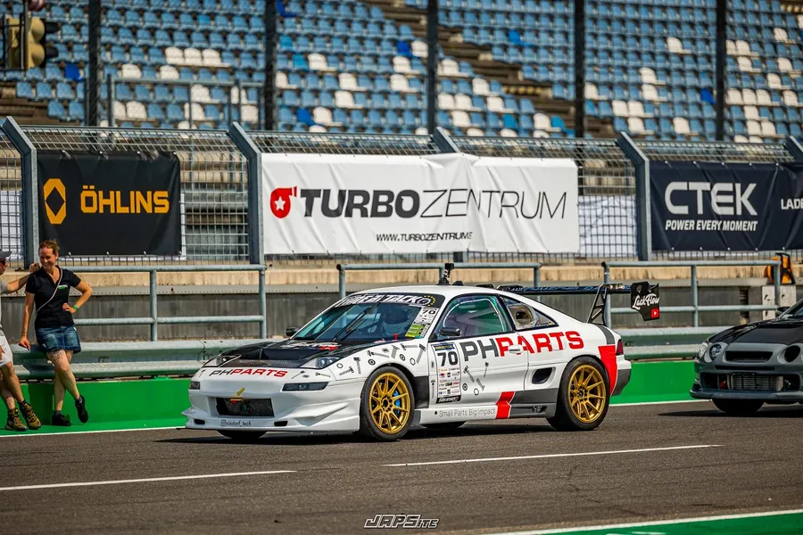 Weißer Toyota MR2 mit der Startnummer 70 rollt durch die Boxengasse, im Hintergrund Werbebanden und leere Tribünenplätze