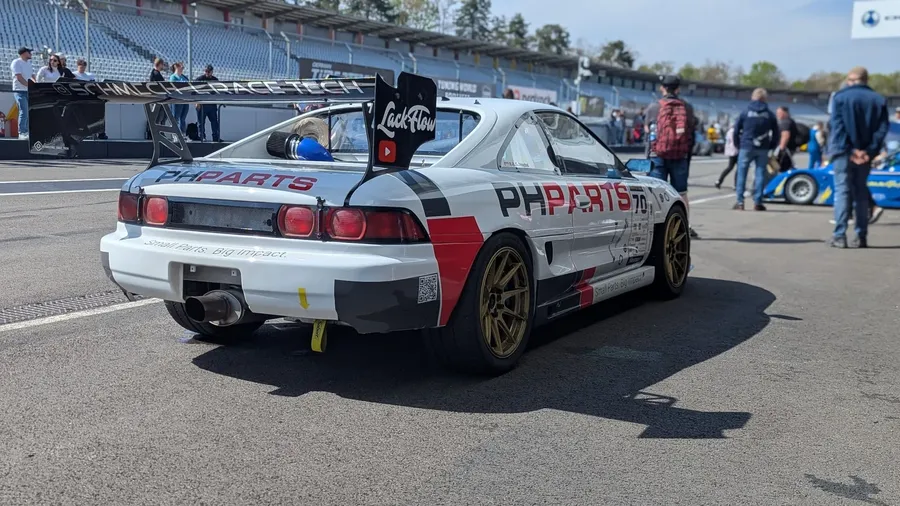Weißer Toyota MR2 mit der Startnummer 70 und großem Heckflügel von schräg hinten in der Startaufstellung, dahinter Zuschauer